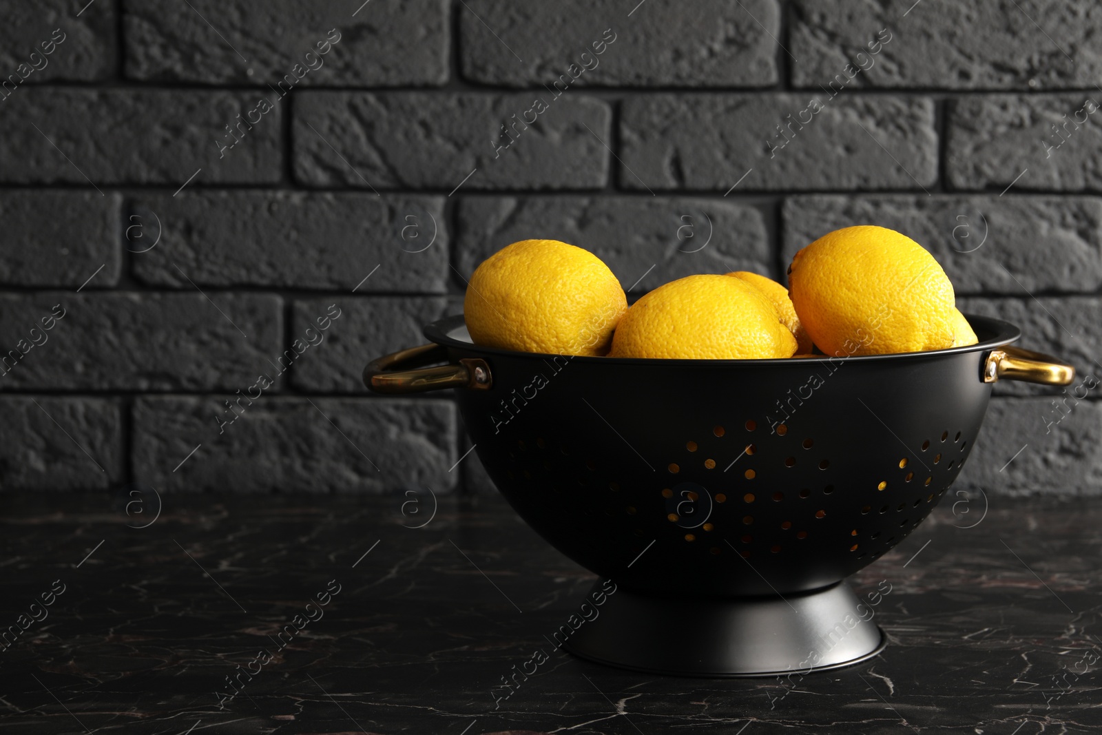 Photo of One colander with fresh lemons on black marble table, space for text