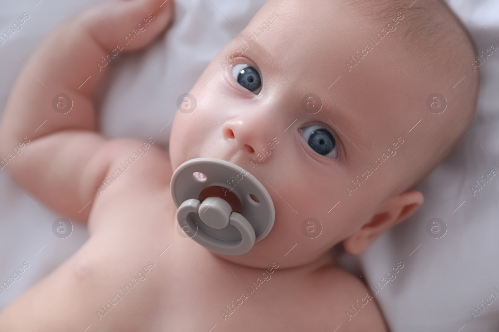 Photo of Cute little baby with pacifier lying on bed, closeup