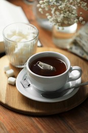 Tray with cup of freshly brewed tea and sugar cubes on wooden table