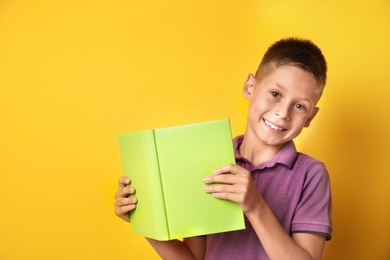 Image of Happy little boy with book on yellow background