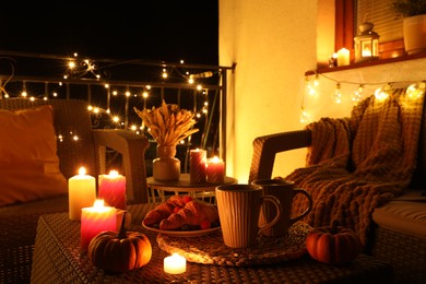 Photo of Rattan furniture, cups, fairy lights, burning candles and other autumn decor on outdoor terrace at night