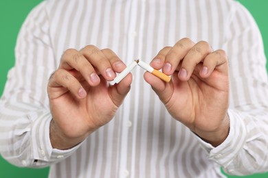 Photo of Stop smoking concept. Man breaking cigarette on green background, closeup