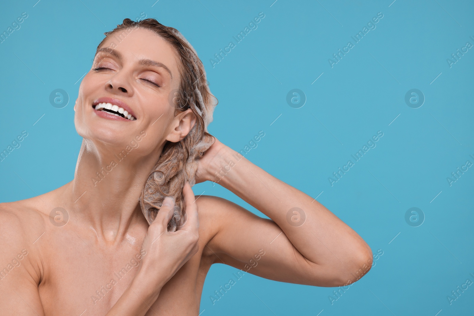 Photo of Portrait of beautiful happy woman washing hair on light blue background. Space for text