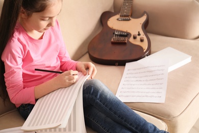 Photo of Little girl with guitar writing music notes at home