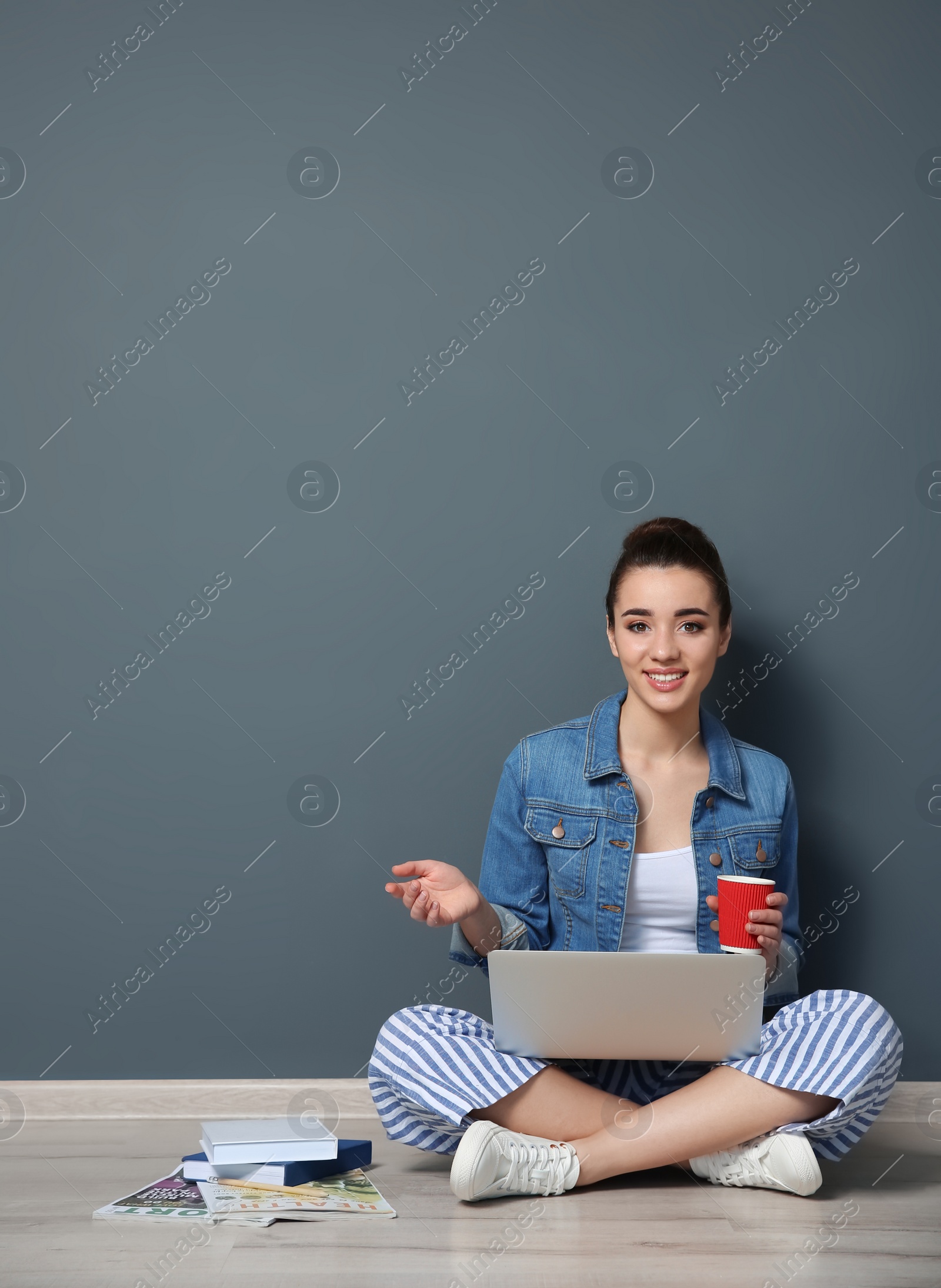 Photo of Young blogger with laptop sitting on floor near color wall
