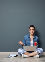 Young blogger with laptop sitting on floor near color wall