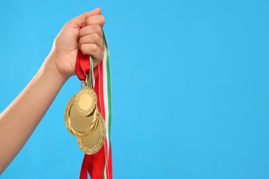 Photo of Woman holding gold medals on light blue background, closeup. Space for text