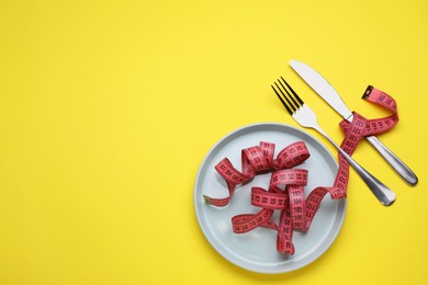 Photo of Measuring tape, fork and knife on yellow background, flat lay with space for text. Weight loss concept