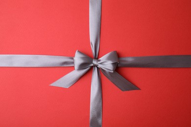 Photo of Grey satin ribbon with bow on red background, top view