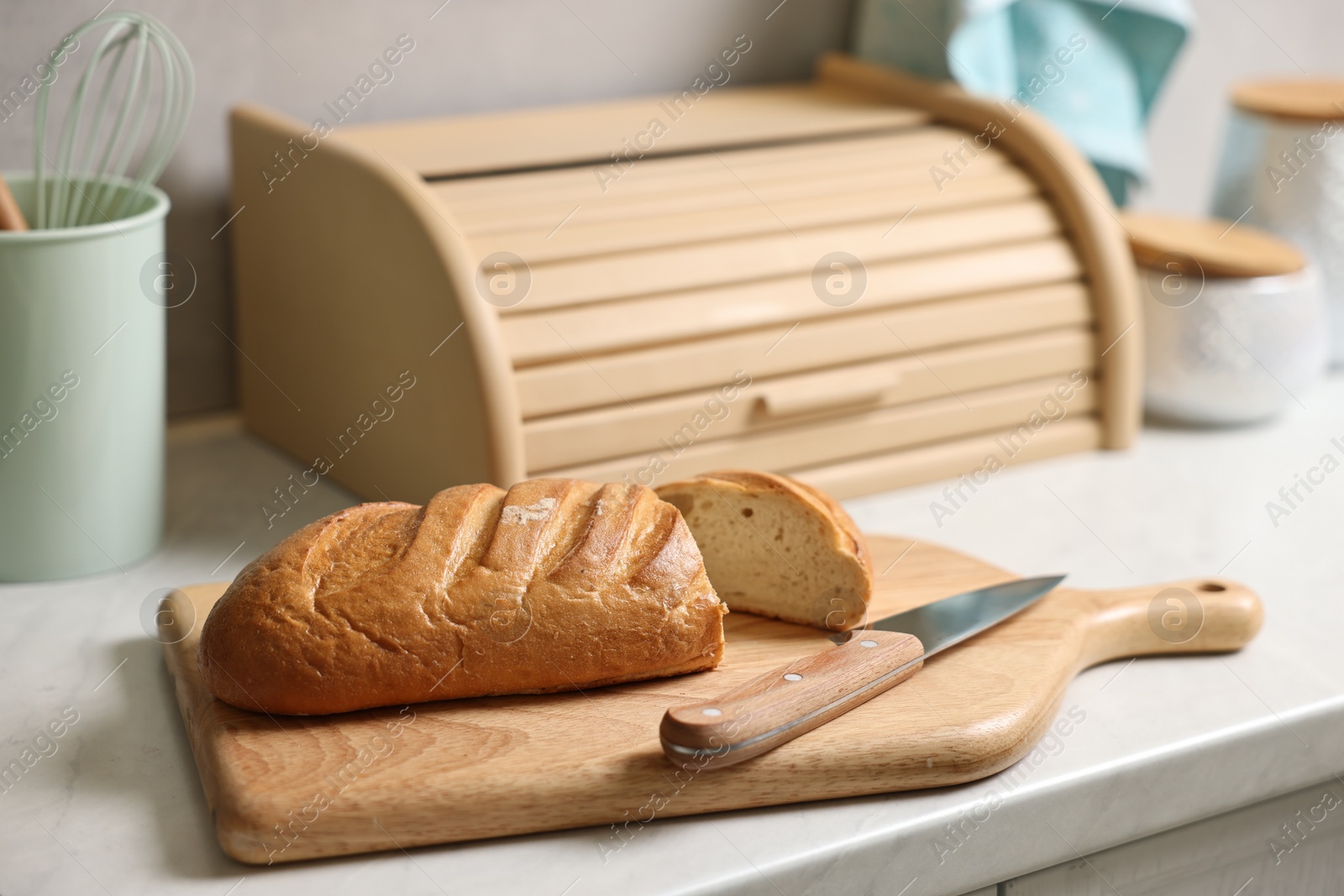 Photo of Wooden bread basket, freshly baked loaf on white marble table in kitchen