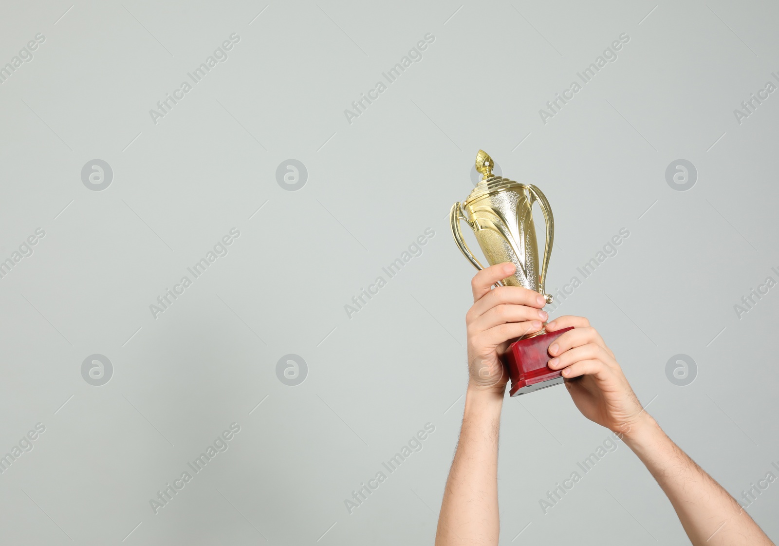 Photo of Man holding gold trophy cup on light grey background, closeup. Space for text