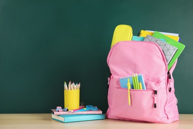 Photo of Color backpack and stationery on table near chalkboard with space for text. Ready for school