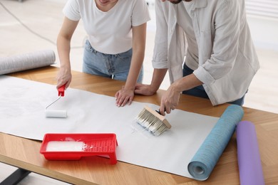 Woman and man applying glue onto wallpaper sheet at wooden table indoors, closeup