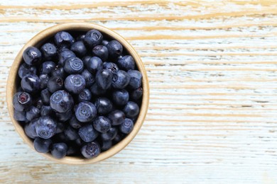 Photo of Tasty fresh bilberries in bowl on old light blue wooden table, top view. Space for text