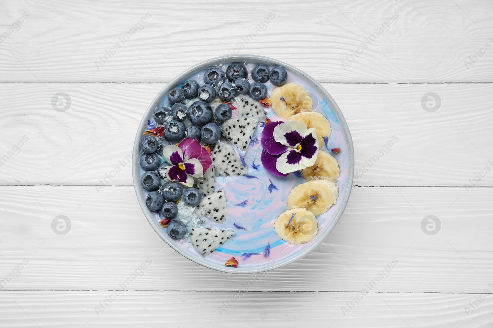 Photo of Delicious smoothie bowl with fresh fruits, blueberries and flowers on white wooden table, top view