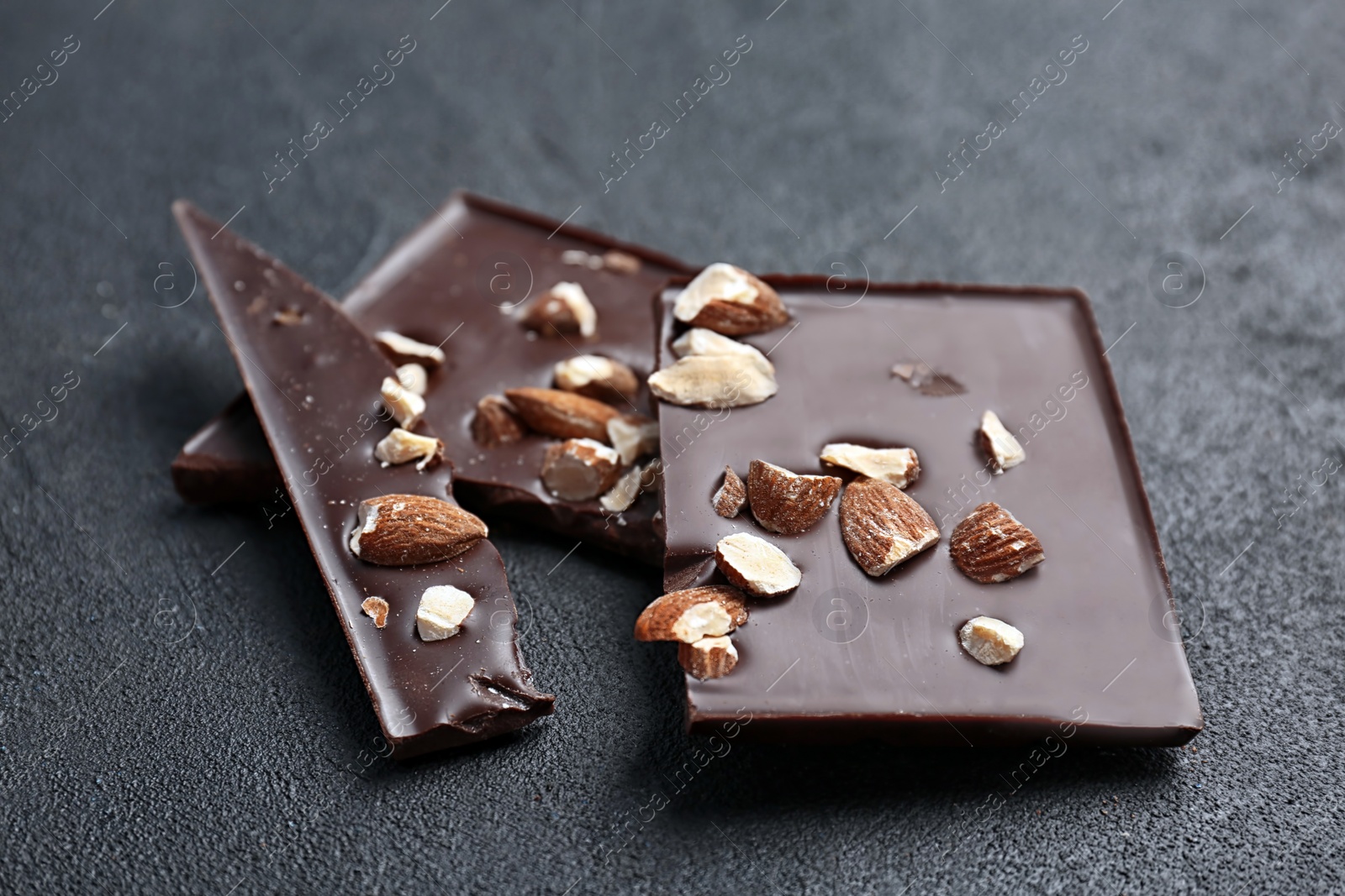 Photo of Delicious broken chocolate bar with nuts on dark table