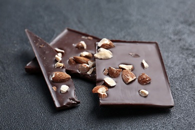 Photo of Delicious broken chocolate bar with nuts on dark table