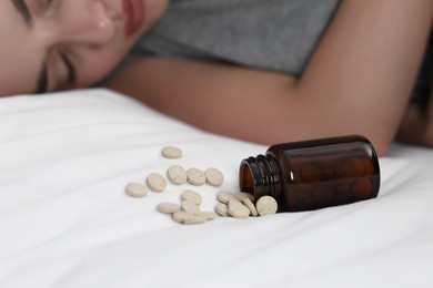 Photo of Woman sleeping on bed near overturned bottle with antidepressants, closeup