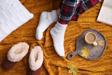 Woman relaxing with cup of hot winter drink on knitted plaid, top view. Cozy season