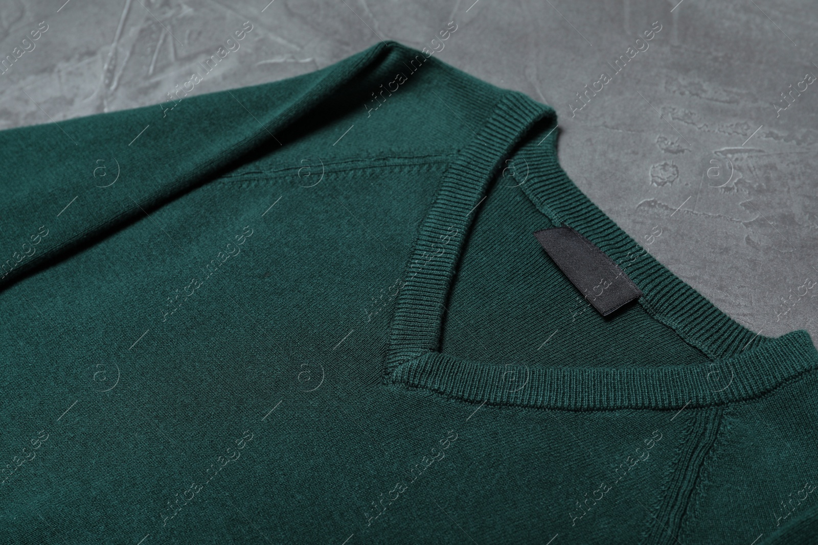 Photo of Green sweater on grey background, closeup. New stylish school uniform