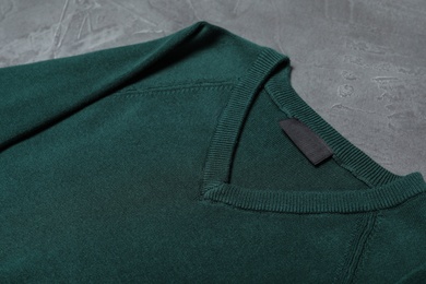 Green sweater on grey background, closeup. New stylish school uniform