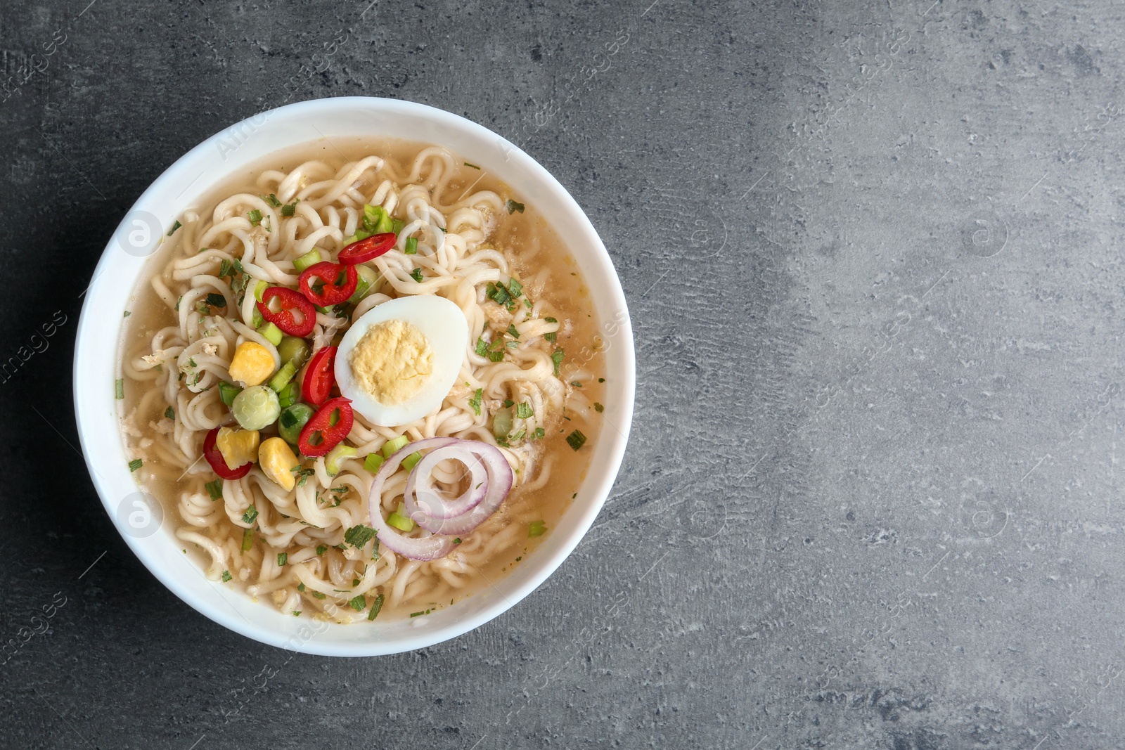 Photo of Bowl of noodles with broth, egg and vegetables on grey background, top view. Space for text