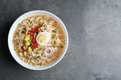 Photo of Bowl of noodles with broth, egg and vegetables on grey background, top view. Space for text