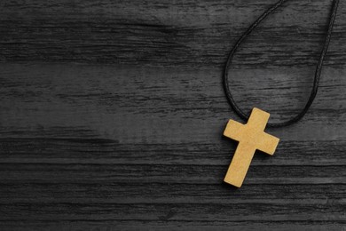 Photo of Christian cross on black wooden table, top view. Space for text