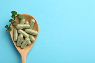 Vitamin capsules and green branch in spoon on light blue background, top view. Space for text