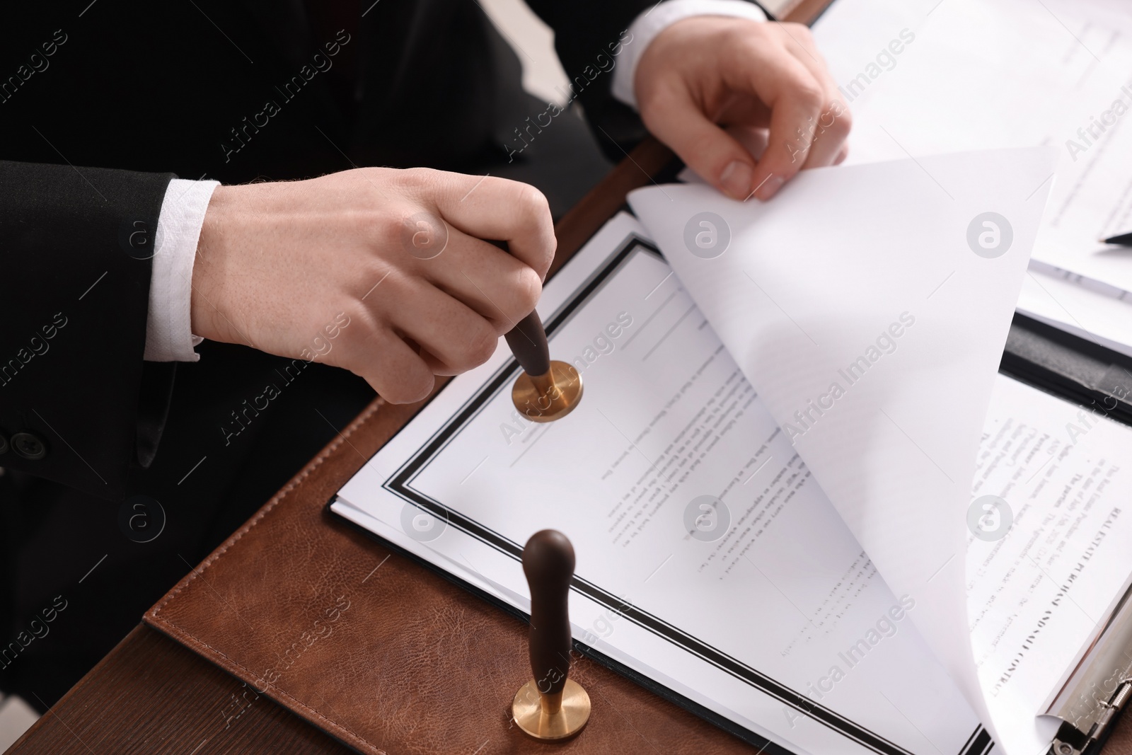 Photo of Notary stamping document at wooden table in office, closeup