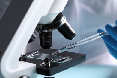 Doctor dripping liquid from pipette onto glass slide on microscope, closeup. Laboratory analysis