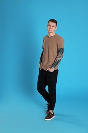 Photo of Smiling young man with tattoos on light blue background