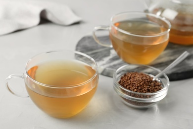 Photo of Glass cup of buckwheat tea and granules on light grey table