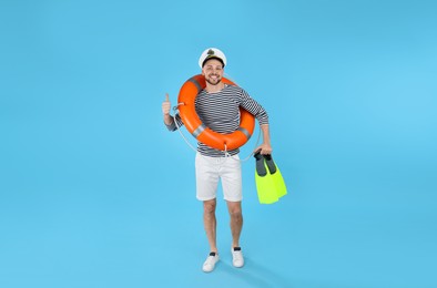 Photo of Happy sailor with orange ring buoy and swim fins on light blue background