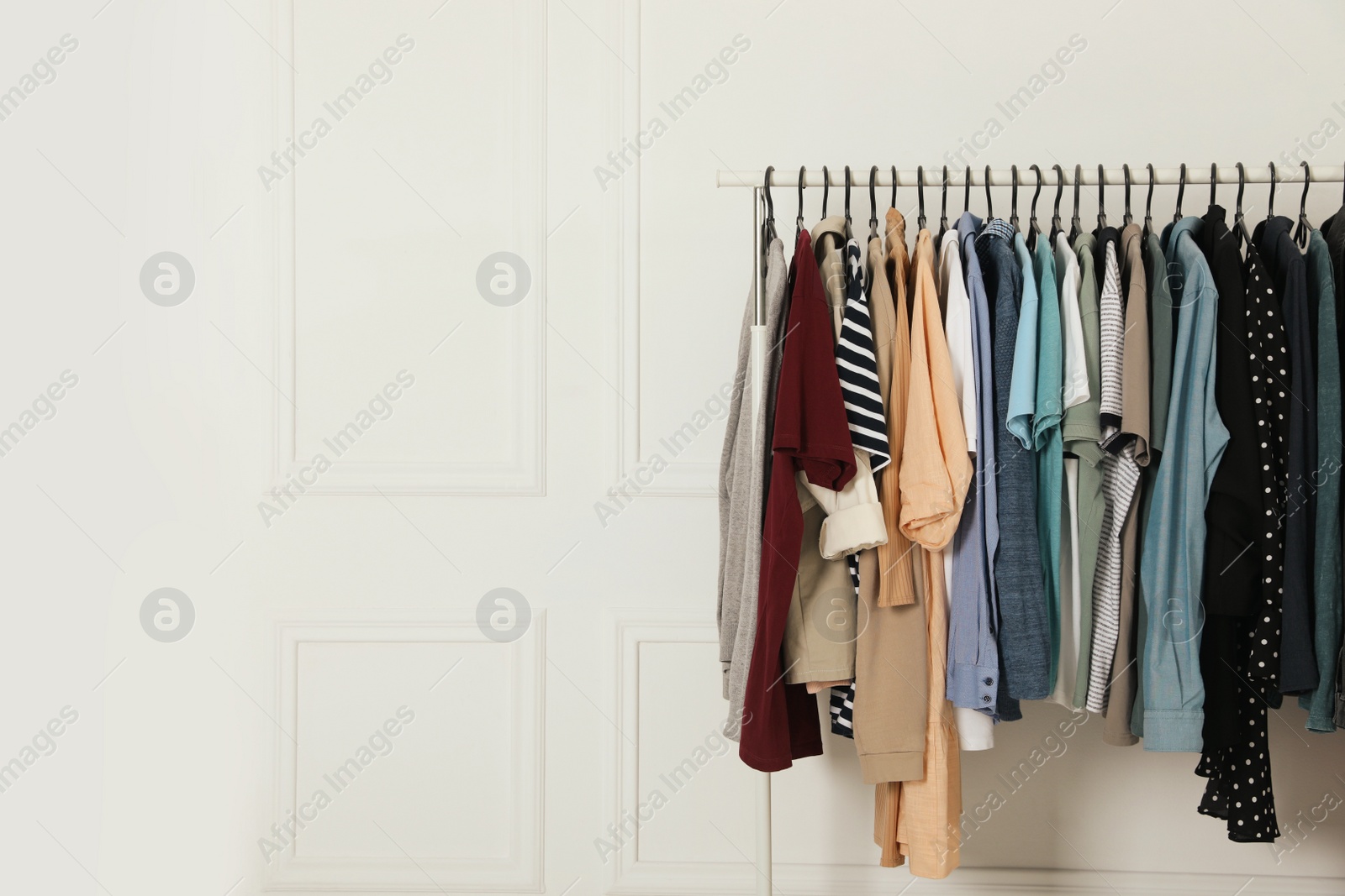 Photo of Rack with stylish clothes near white wall indoors. Fast fashion