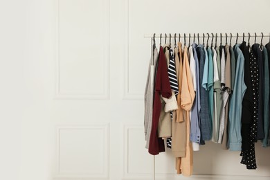 Rack with stylish clothes near white wall indoors. Fast fashion