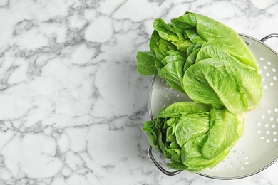 Photo of Colander with fresh ripe cos lettuce on marble table, top view