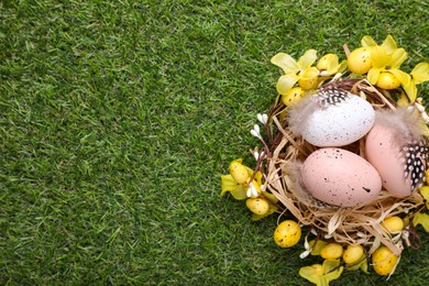 Photo of Festively decorated Easter eggs on green grass, top view. Space for text