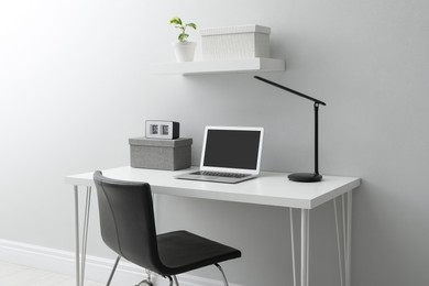 Photo of Stylish workplace with laptop and comfortable chair near white wall indoors. Interior design