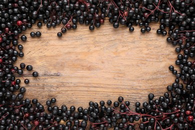 Photo of Frame of black elderberries (Sambucus) on wooden table, flat lay. Space for text