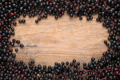 Frame of black elderberries (Sambucus) on wooden table, flat lay. Space for text