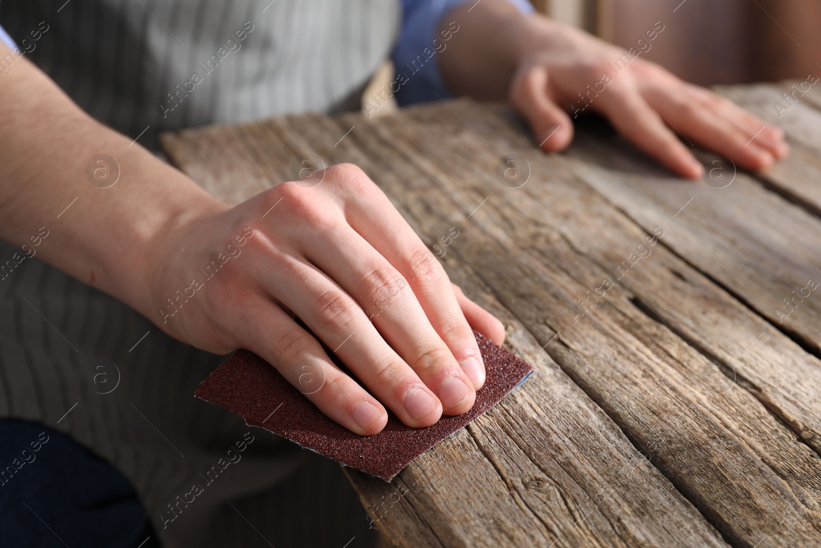 Photo of Man polishing wooden table with sandpaper indoors, closeup