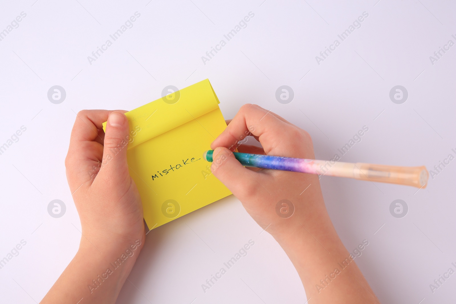 Photo of Child erasing word Mistake written with erasable pen on sticky note against white background, top view