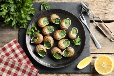 Delicious cooked snails served on wooden table, flat lay