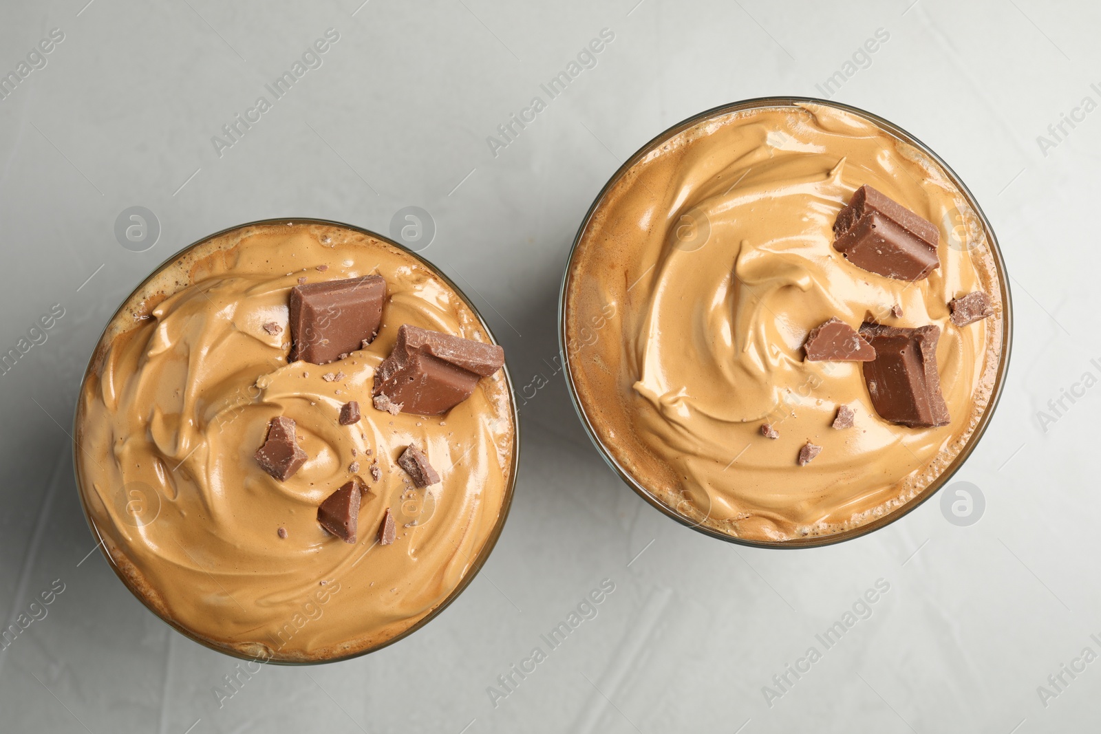 Photo of Glasses of delicious dalgona coffee with chocolate on light grey table, flat lay