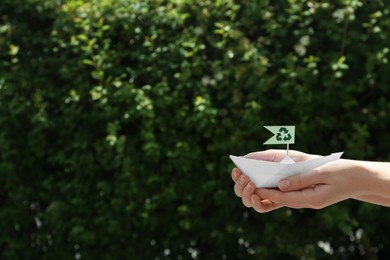 Woman holding paper boat with recycling symbol outdoors, closeup. Space for text