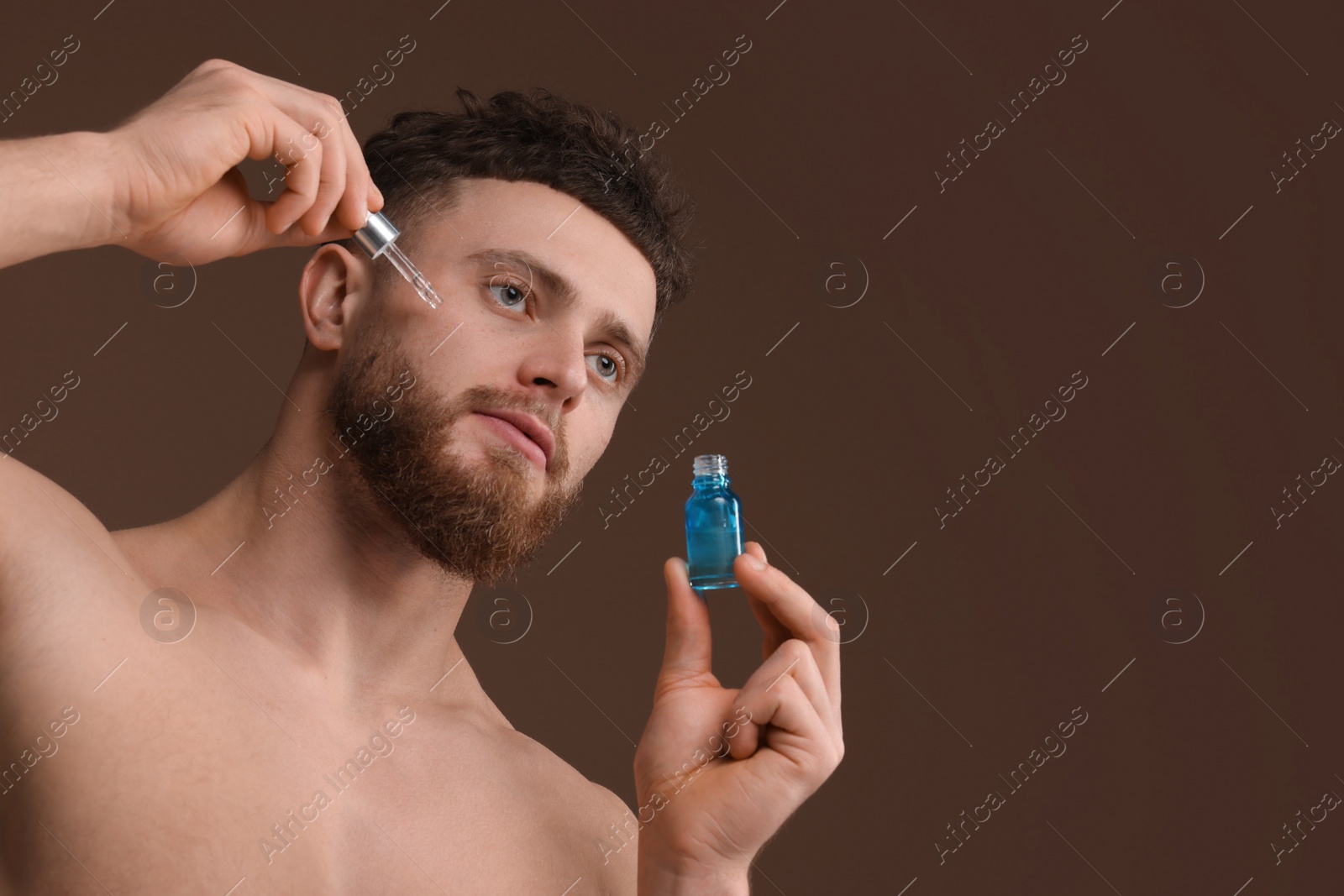 Photo of Handsome man applying serum onto his face on brown background, space for text