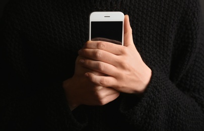 Photo of Lonely woman holding smartphone on black background, closeup