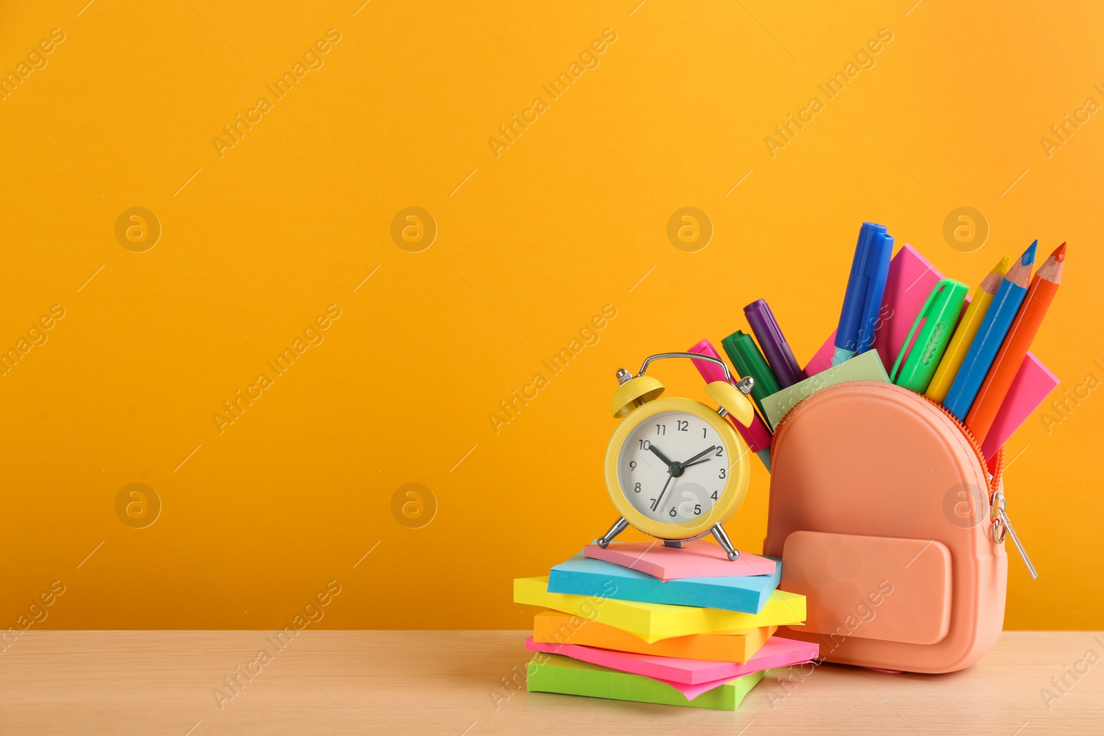 Photo of Different school stationery and alarm clock on table against orange background, space for text. Back to school