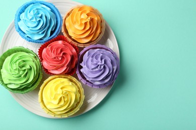 Photo of Plate with delicious bright cupcakes on turquoise background, top view. Space for text